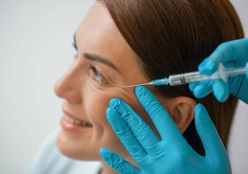 Crawley Botox Treatment where woman is joyfully receiving her treatment with a doctor's hands pressed against her cheek and syringe on her temple